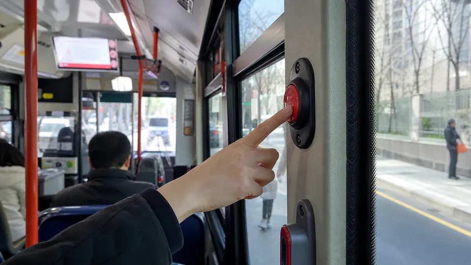 Illustrated hand pressing a red stop-request button inside a Seoul city bus